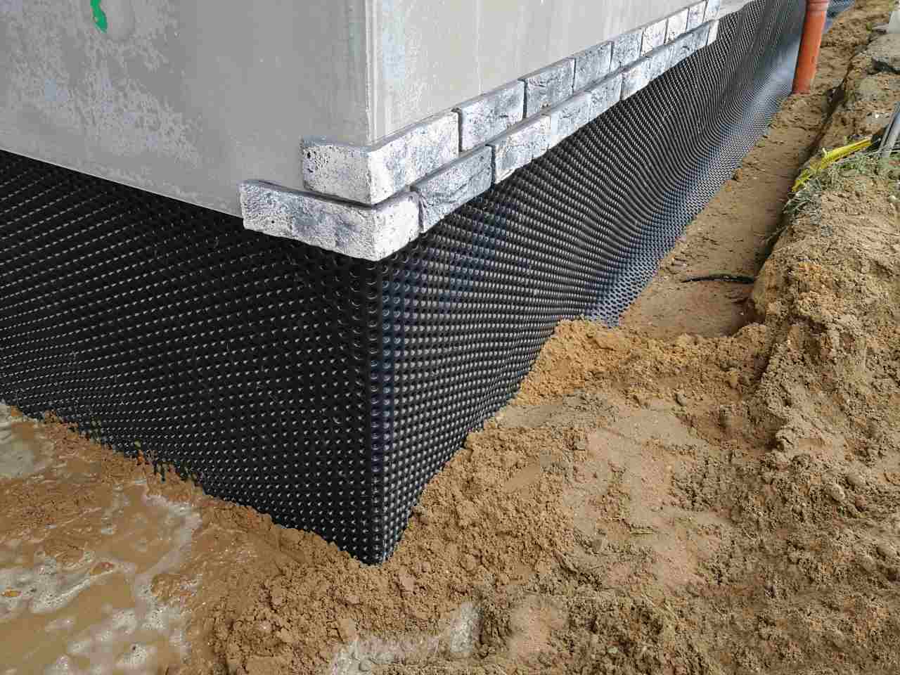 Black plastic drainage membrane installed on foundation wall for waterproofing